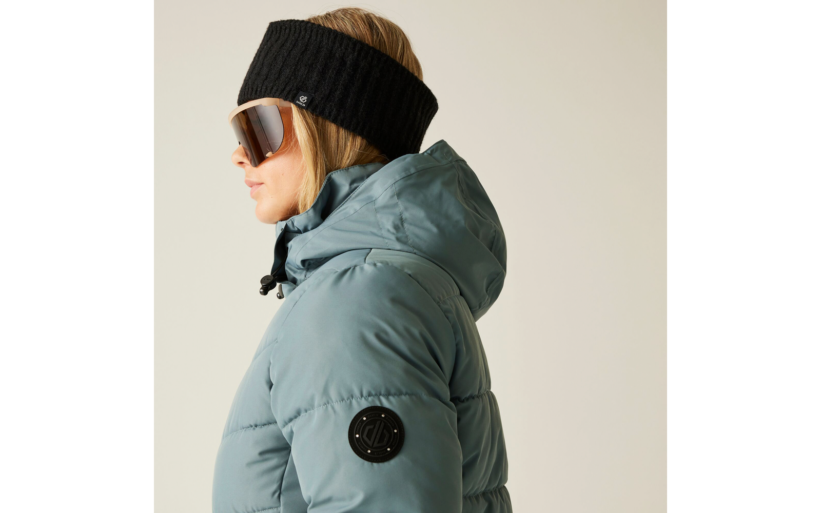 Frau seitlich, trägt eine dicke Steppjacke, Stirnband und Sonnenbrille