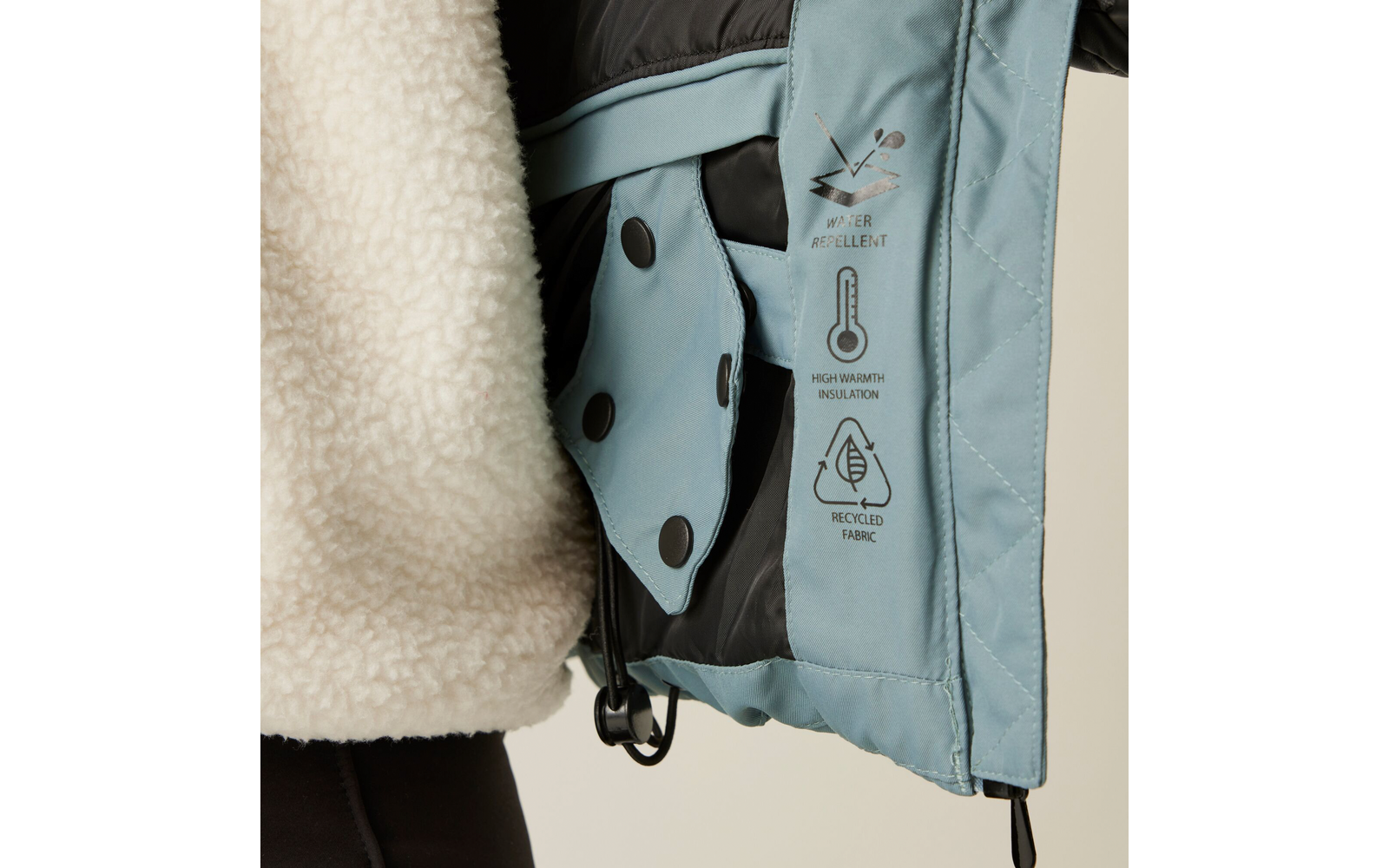 Nahaufnahme des Innenfutters und der Etiketten einer hellblauen Jacke mit Teddyfellstoff an der Außenseite