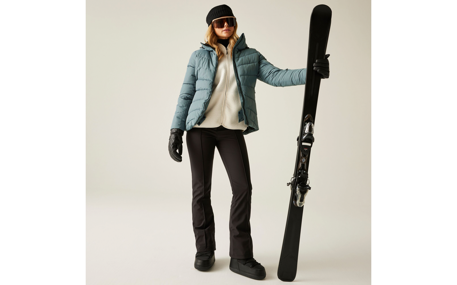 Vrouw staat met ski's in de hand voor een lichte achtergrond