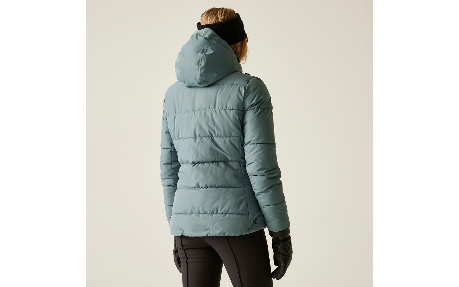Person von hinten in blauer Steppjacke mit Kapuze, steht vor hellem Hintergrund