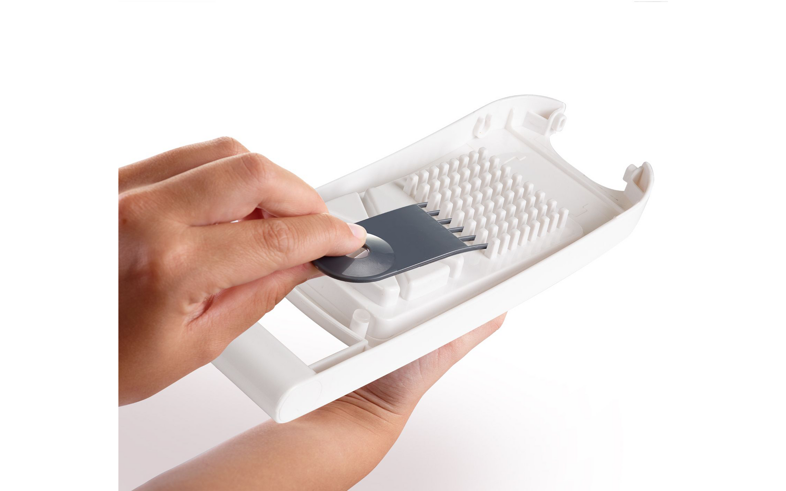 Two hands hold a white plastic device; one hand places a gray metal blade into a slot with plastic spikes