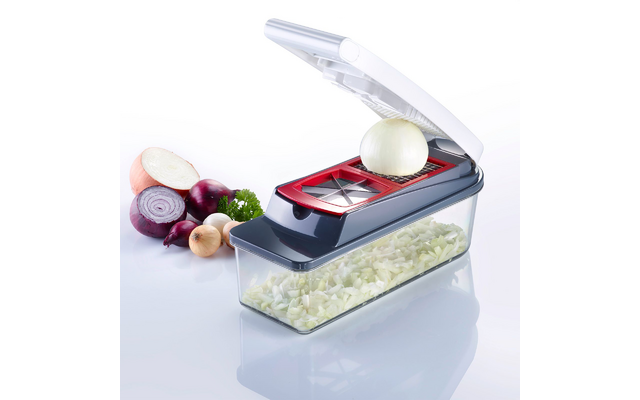 Plastic device with open white lid, red blade frame and transparent container holding chopped onion pieces; to the left halved and whole onions and a parsley sprig on a white background