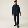 Mann steht, trägt dunkelblaue Outdoorjacke, blaugrünes T‑Shirt, dunkelblaue Hose und schwarze Wanderschuhe mit grünen Details; schaut nach rechts