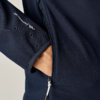 Hand steckt in Reißverschlusstasche einer dunkelblauen Jacke, weißer Reißverschluss und weißes Logo auf dem Ärmel
