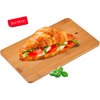 Croissant sandwich filled with tomato slices, white cheese slices and green leaves on a wooden cutting board; a few loose green leaves beside it; red label '25 x 15 cm' at top left