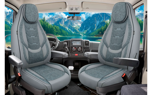 Innenraum eines Fahrzeugs mit zwei grauen Vordersitzen mit Armlehnen und Sicherheitsgurten, Armaturenbrett und Lenkrad, Blick durch die Windschutzscheibe auf einen türkisfarbenen See und bewaldete, schneebedeckte Berge