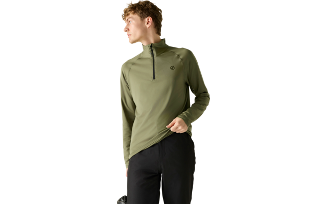 Personne portant un haut manches longues olive avec une courte fermeture éclair et petit logo, pantalon noir, regardant vers la gauche et tenant l'ourlet de la main droite, fond clair