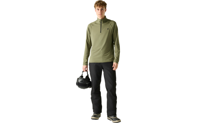 Personne debout portant un haut manches longues olive avec une courte fermeture éclair et un pantalon noir, tenant un casque noir dans la main droite sur un fond uni clair