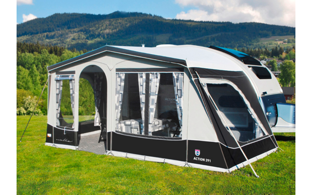 Schwarzes und weißes Wohnmobilzelt auf einer grünen Wiese mit Bergen im Hintergrund