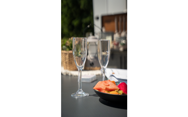 Twee gevulde champagneglazen op een tafel naast een kom met meloenstukken buiten