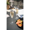 Twee gevulde champagneglazen op een wit gedekte tafel naast een zwart bord met sinaasappelschijfjes en een vaas met gedroogde bloemen