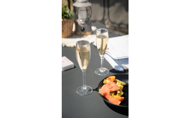Twee gevulde champagneglazen op een wit gedekte tafel naast een zwart bord met sinaasappelschijfjes en een vaas met gedroogde bloemen