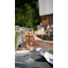 Hand houdt een glas met bruisend drankje vast, op de achtergrond meer glazen en een onscherpe buitenomgeving