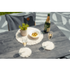 Table en bois gris avec deux flûtes de champagne, une bouteille de champagne ouverte, un bol d'olives sur cure-dents, un petit pot de plante sur un napperon macramé rond, deux sous-verres macramé et une chaise grise en arrière-plan