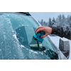 Hand met blauwe ijskrabber verwijdert ijs van de voorruit van een wit voertuig; besneeuwd landschap en bomen op de achtergrond