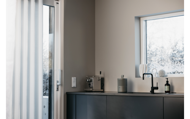 Moderner Innenraum mit schwarzem Sideboard, darauf Kerzen und Dekoration, Fenster mit Blick auf verschneite Bäume
