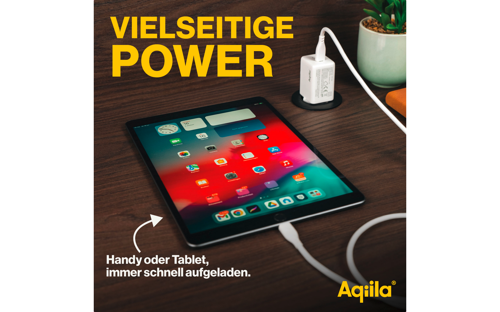 Tablet auf einem Tisch, daneben ein USB-Ladegerät und eine Pflanze