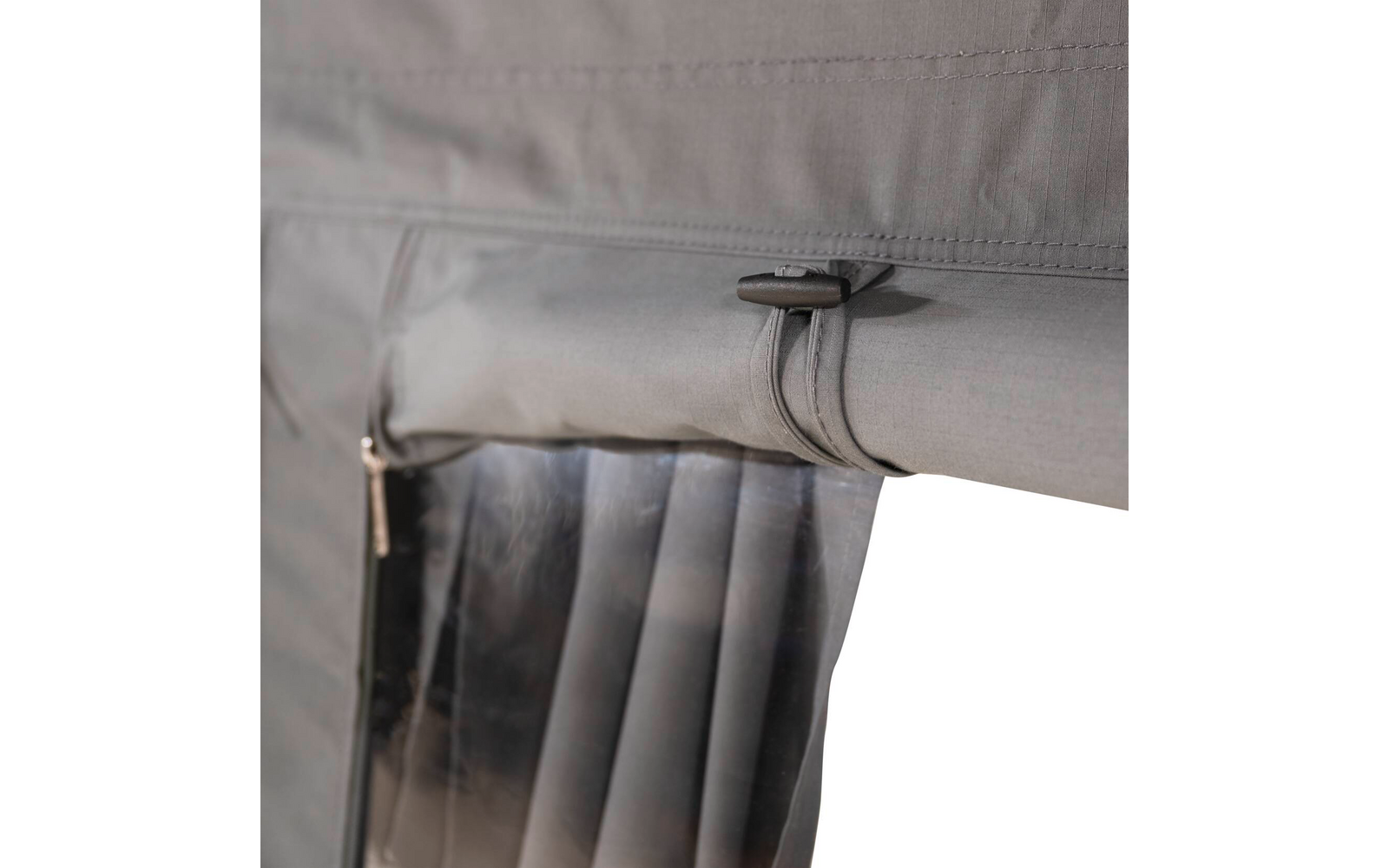 Grauer Stoff mit aufgerolltem transparentem Kunststoffvorhang, befestigt durch einen Gurt mit Schlaufe; links ein sichtbarer Reißverschluss