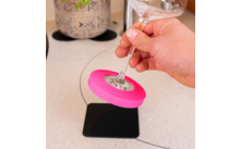 Hand hält den Stiel eines Weinglases mit einem pinken Silikonring um den Boden des Glases