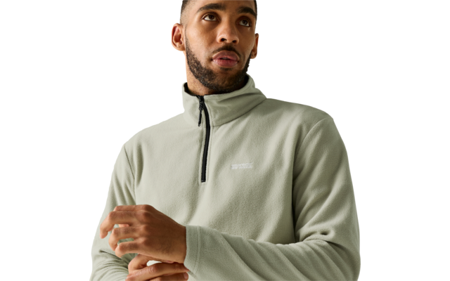 Person, chest-up view, wearing light green fleece with stand collar and half zipper, short hair, short beard, hands near chest, looking up and to the right, white background