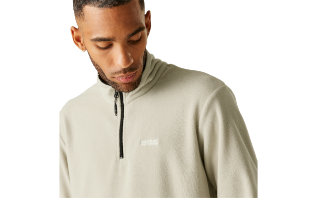 Person looking down, wearing a light beige quarter-zip fleece with a small white chest logo