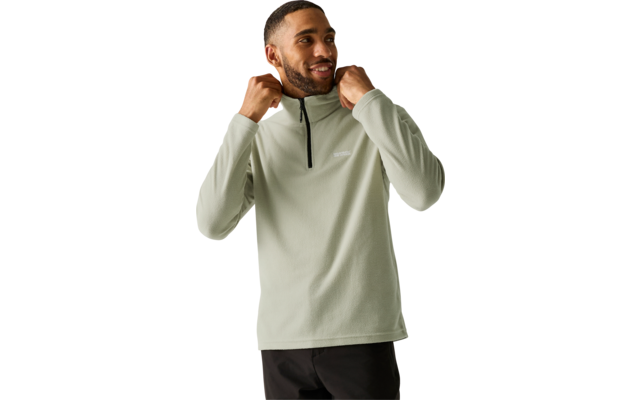 Man in light sage-green fleece pullover with short zipper, hands at collar, smiling