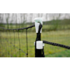 Black braided rope threaded through white plastic clips on a post, fence netting to the left, blurred grassy field in the background
