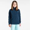 Junges Mädchen steht vor weißem Hintergrund, trägt blauen Pullover und helle Hose