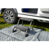 Zweistufige schwarze Trittstufe auf grauem, gemustertem Teppich vor geöffneter Seitentür eines weißen Fahrzeugs; Fahrzeugrad und Gras sichtbar