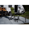 Grüner Campingstuhl mit passendem Fußhocker auf gemusterter Outdoor-Matte vor geöffneter Tür eines Wohnmobils; Outdoor-Küchenzeile links sichtbar