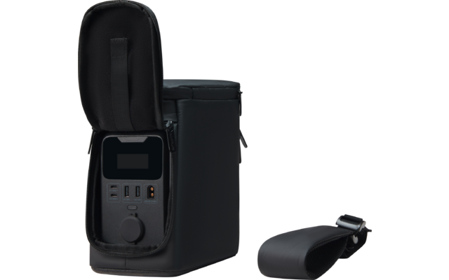 Zwarte rechthoekige tas met geopend voorvak; binnenin een donker rechthoekig schermgebied en meerdere aansluitopeningen (rechthoekig en rond). Rechts ligt een losgemaakt, gewatteerd zwart schouderkussen met metalen gesp