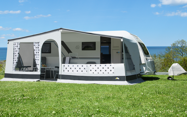 Caravane avec auvent attaché sur de l'herbe verte, ciel bleu et mer en arrière-plan