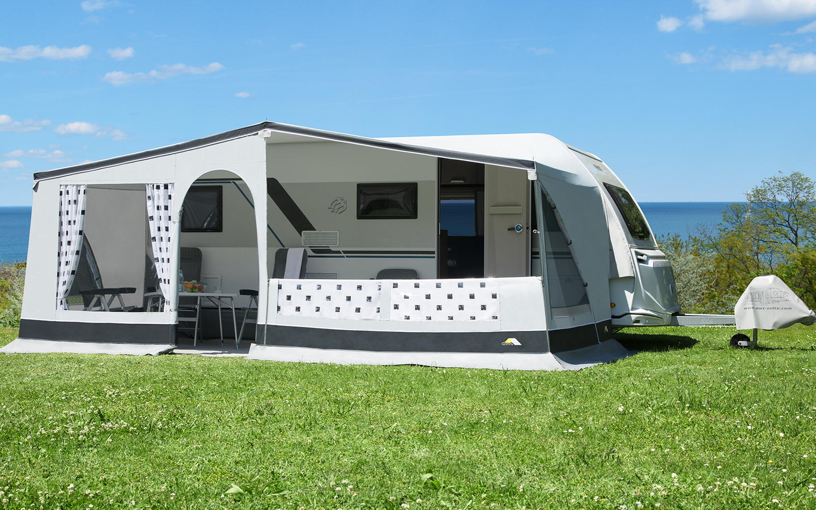Caravane avec auvent attaché sur de l'herbe verte, ciel bleu et mer en arrière-plan