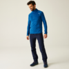 Mann mit blauem Pullover und dunkler Hose steht vor heller Wand
