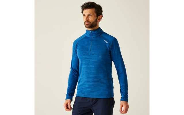 Mann mit dunklem Bart trägt blauen Pullover vor hellem Hintergrund