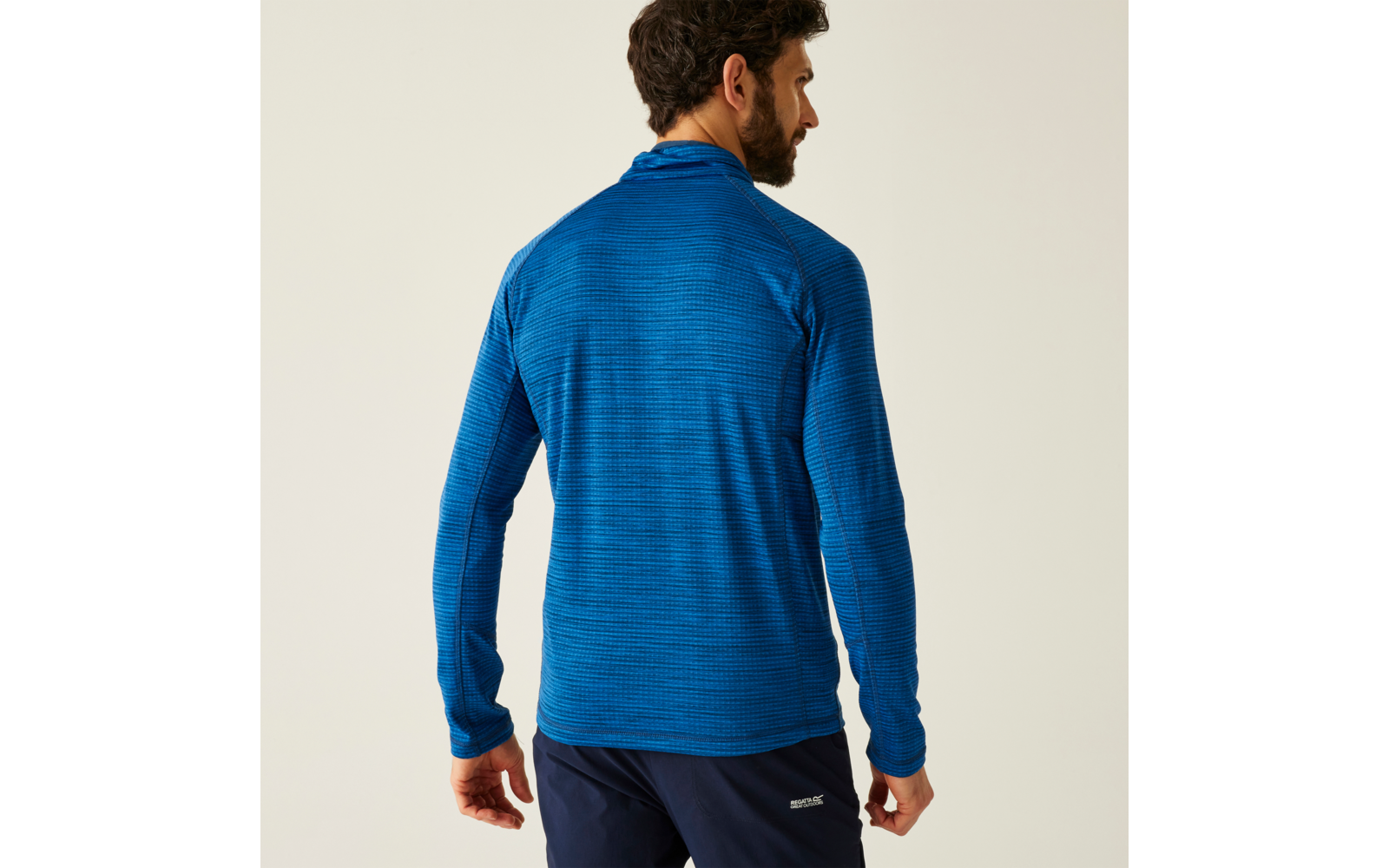 Mann von hinten mit blauem Pullover und dunkler Hose vor weißem Hintergrund