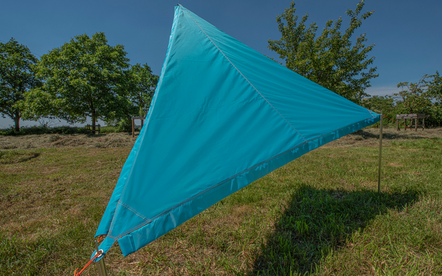 Blaues, dreieckiges Segel vor blauem Himmel auf einer grünen Wiese mit Bäumen im Hintergrund
