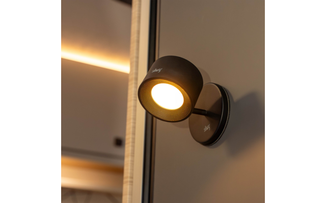 Schwarze, runde Wandlampe eingeschaltet mit warmem Licht, montiert neben einem Spiegel