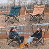 Zwei Outdoor-Stühle auf einer Wiese mit kahlen Bäumen im Hintergrund. Männer sitzen jeweils auf einem Stuhl