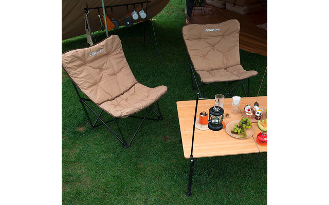 Zwei beige Campingstühle auf grünem Rasen neben einem Holztisch mit Getränkedosen und Spielzeug