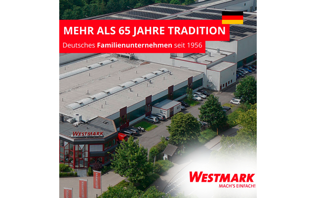 Vue aérienne d'un bâtiment industriel aux toits plats avec panneaux solaires, entrée vitrée rouge portant l'inscription 'Westmark', voitures et camions garés, arbres ; bannière rouge avec le texte 'MEHR ALS 65 JAHRE TRADITION' et drapeau allemand, ligne 'Deutsches Familienunternehmen seit 1956' ; logo 'WESTMARK MACH'S EINFACH!' en bas à droite