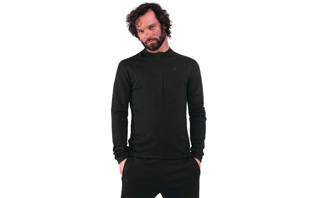 Persona con barba e capelli scuri ricci fino alle spalle, indossa una maglia a maniche lunghe nera e pantaloni neri, mani nelle tasche, sfondo bianco