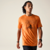 Person mit Dreadlocks trägt ein orangefarbenes T‑Shirt mit Fahrrad- und Bergmotiv vor hellem Hintergrund