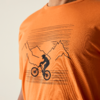 Orangefarbenes T-Shirt mit schwarzem Druck: Silhouette einer Person auf einem Fahrrad vor stilisierten Bergen und waagerechten Linien