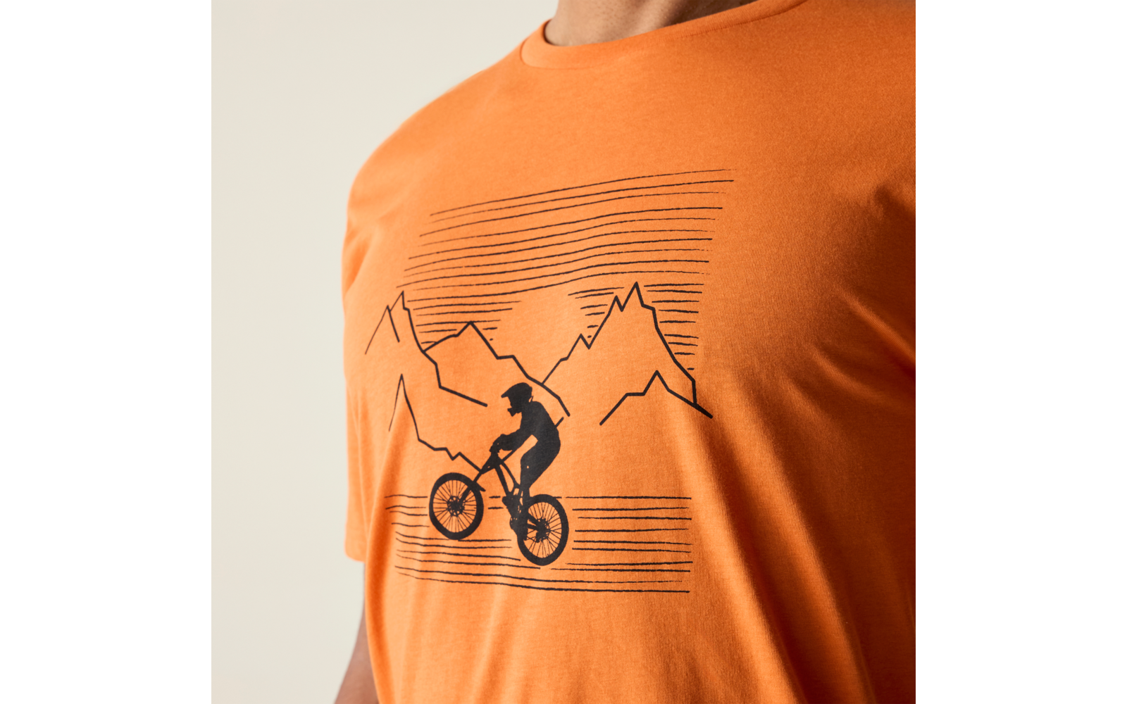 Orangefarbenes T-Shirt mit schwarzem Druck: Silhouette einer Person auf einem Fahrrad vor stilisierten Bergen und waagerechten Linien