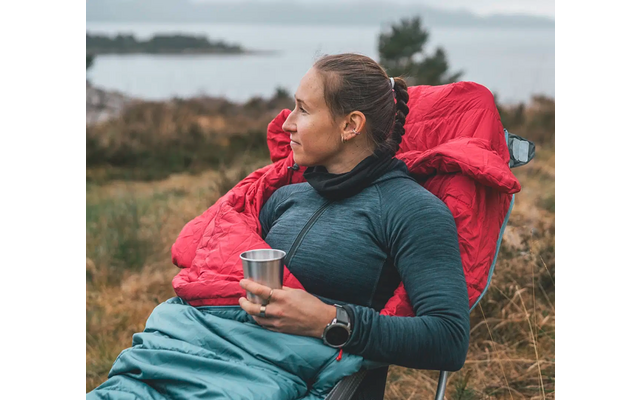 Vrouw zit buiten op gras met een rode rugzak en houdt een kopje in haar hand