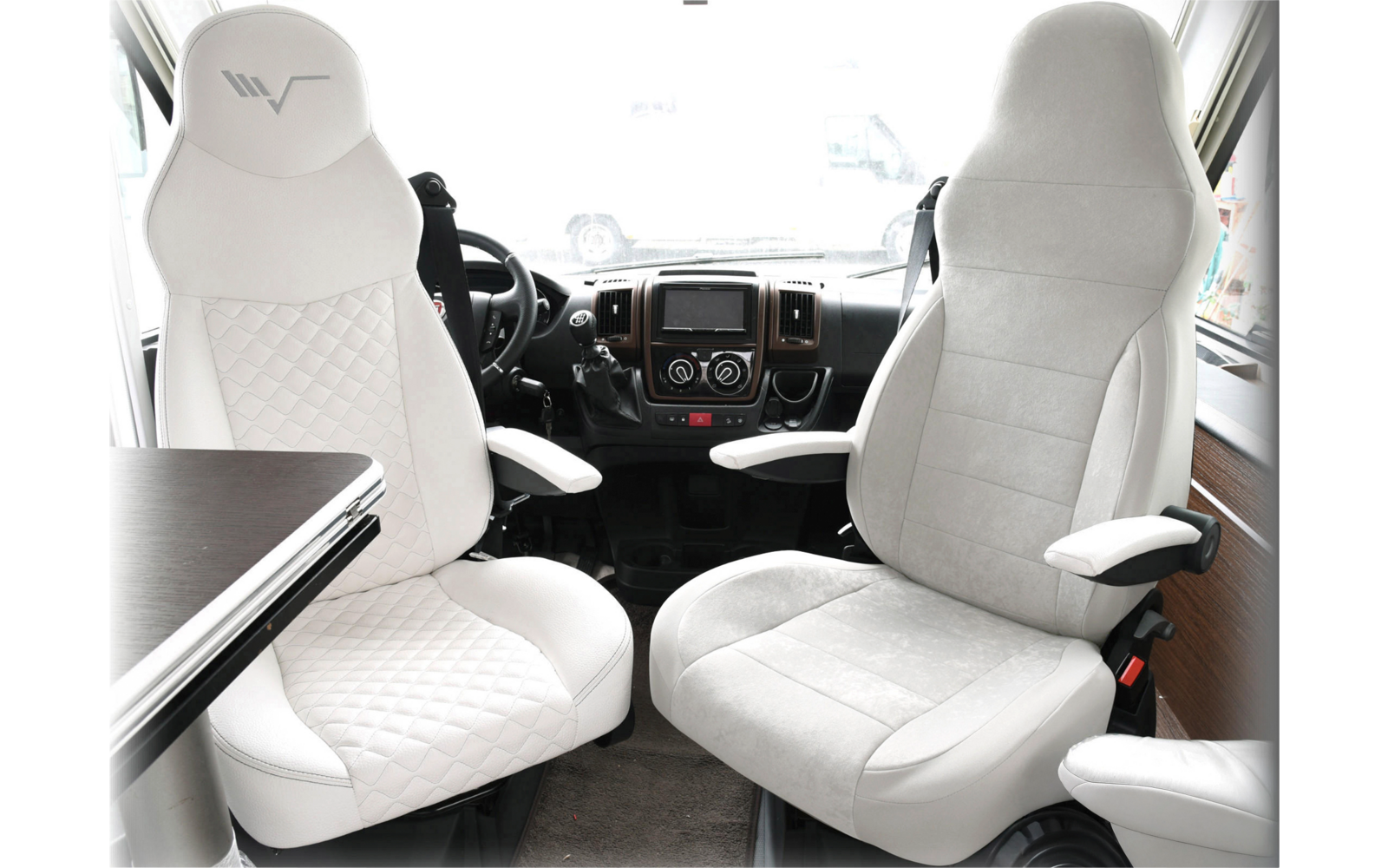 Deux sièges de conducteur blancs et confortables dans un véhicule avec accoudoirs et une table à côté du siège gauche