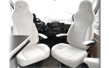 Zwei weiße bequeme Fahrersitze in einem Fahrzeug mit Armlehnen und einem Tisch neben dem linken Sitz