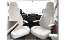 Two white comfortable driver seats in a vehicle with armrests and a table next to the left seat