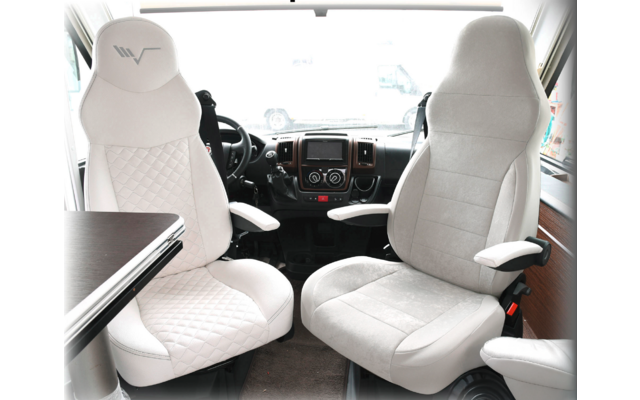 Two white comfortable driver seats in a vehicle with armrests and a table next to the left seat